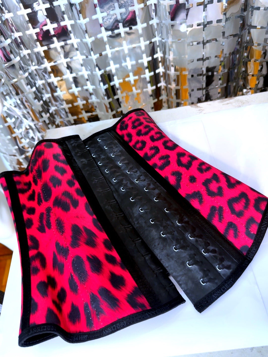 Black and pink leopard print corset belt on a white surface with a reflective background.