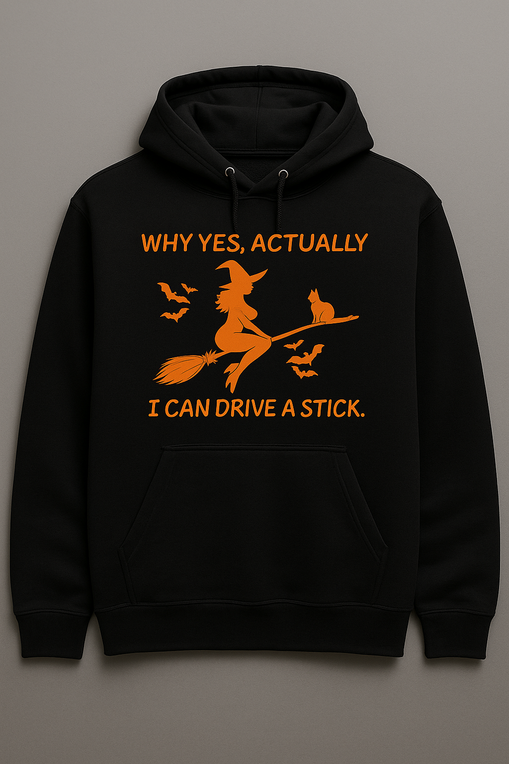 Black hoodie with bold orange witch on a broom, bats, and the phrase ‘I Can Drive a Stick’ in curved lettering.”